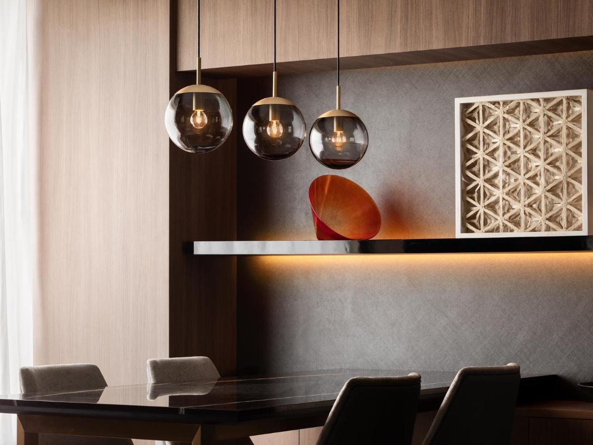 Mitsui Garden Hotel Roppongi Tokyo Premier Экстерьер фото The photo depicts a modern interior design scene. It features a sleek dining area with a dark wooden table and comfortable chairs. Above the table, there are three pendant lights with glass shades that provide ambient lighting. A geometric art piece 