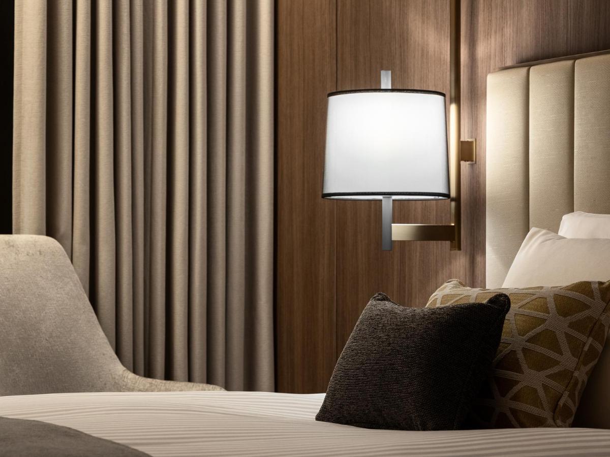 Mitsui Garden Hotel Roppongi Tokyo Premier Экстерьер фото The photo displays a cozy hotel room setting. It features a neatly made bed with white linens and several decorative pillows. To the side, there’s a stylish bedside lamp mounted on the wall with a round white shade. Behind the lamp, there are elegant