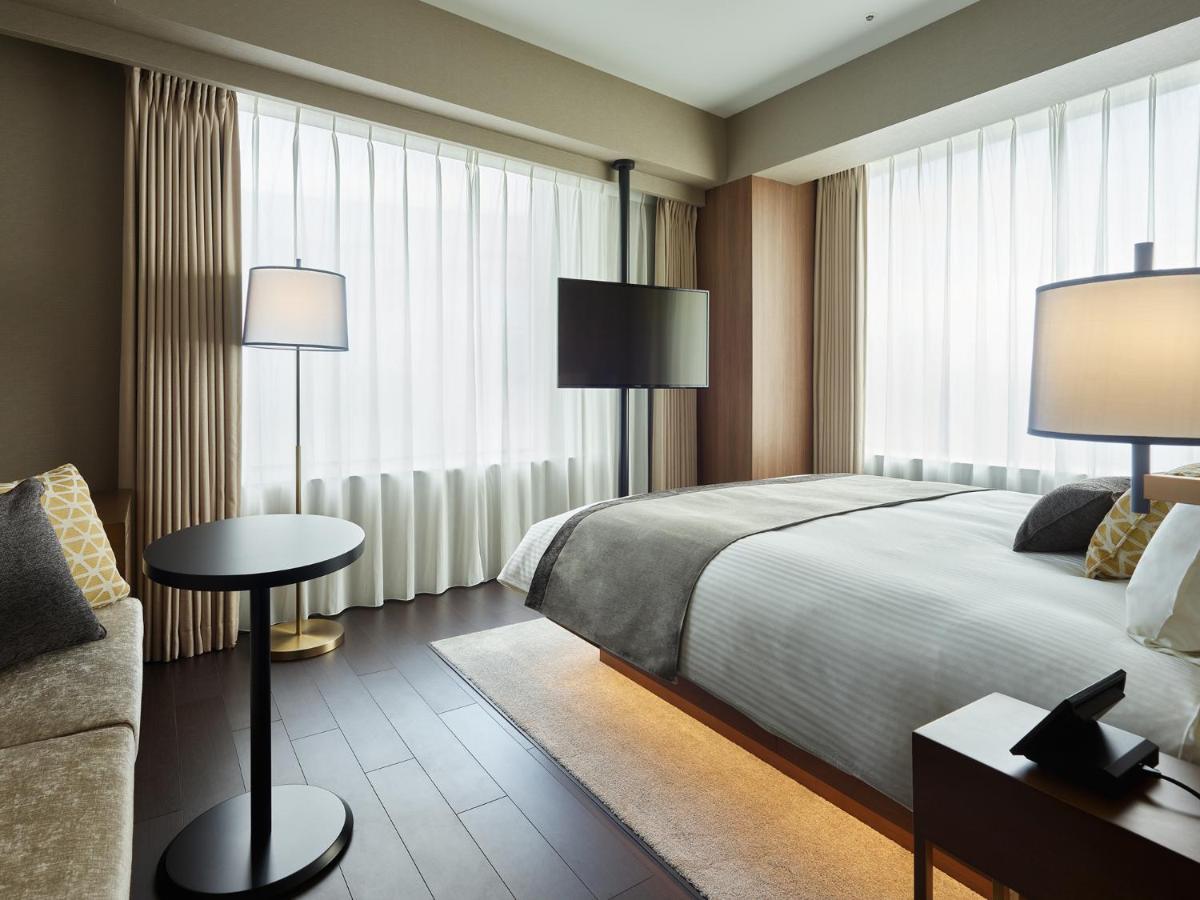 Mitsui Garden Hotel Roppongi Tokyo Premier Экстерьер фото The photo shows a modern hotel room with a contemporary design. It features a large bed with crisp white linens, sitting against a wall with floor-to-ceiling windows covered by sheer curtains, allowing natural light to filter in. To the side, there's