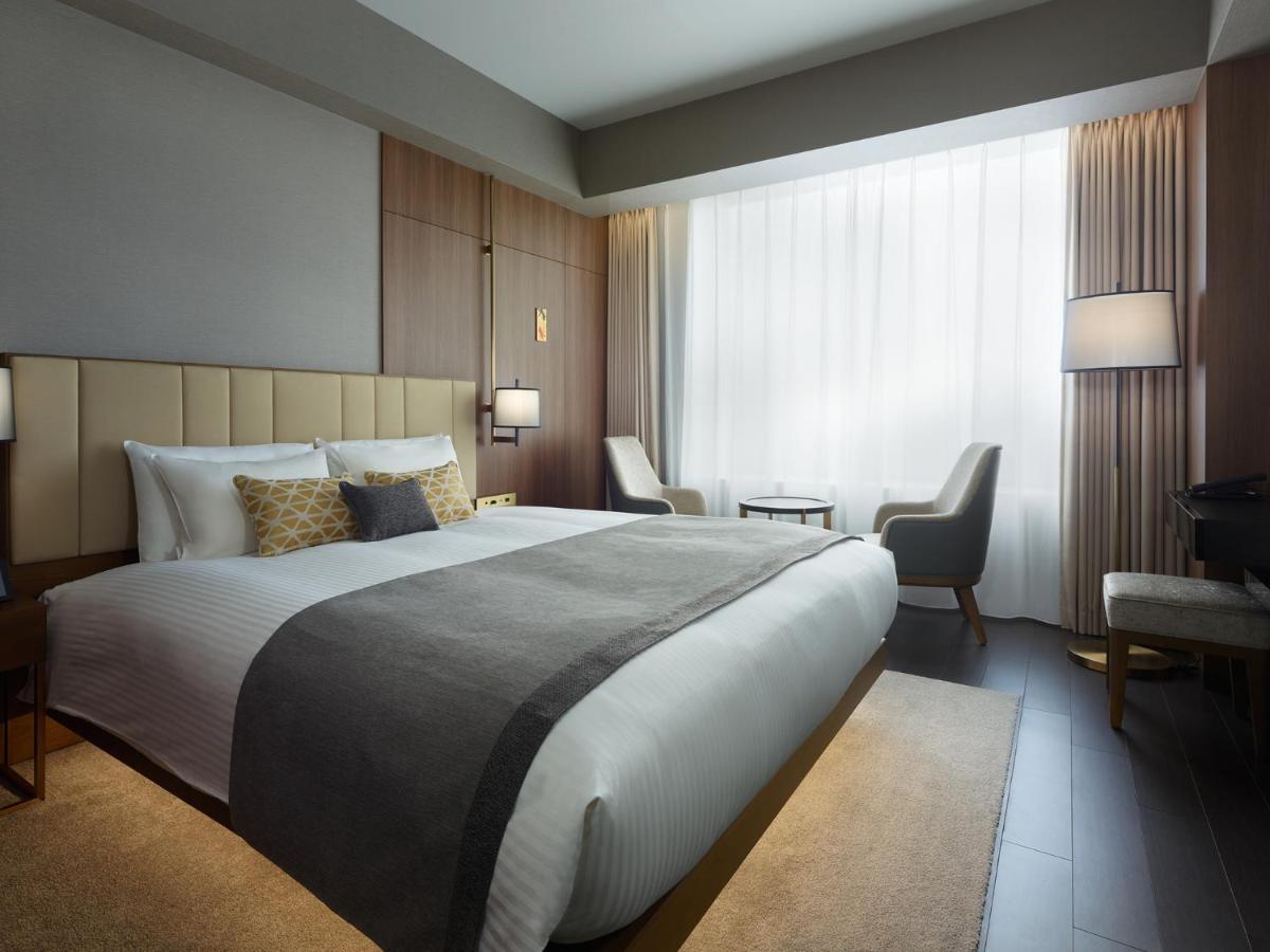 Mitsui Garden Hotel Roppongi Tokyo Premier Экстерьер фото The photo shows a modern hotel room featuring a large bed with a neatly arranged white and gray bedding. The headboard is upholstered in a light color, adding to the room's contemporary design. On either side of the bed, there are bedside lamps provi