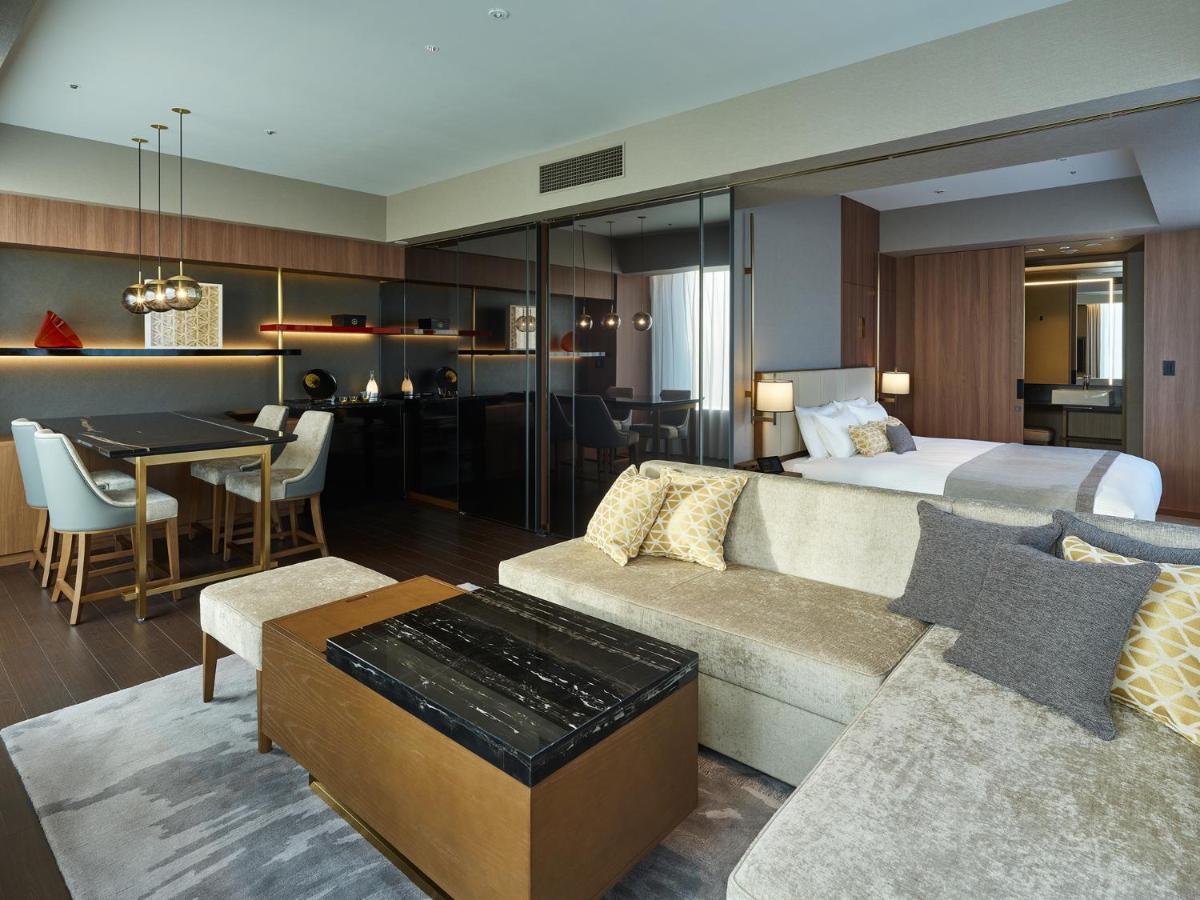 Mitsui Garden Hotel Roppongi Tokyo Premier Экстерьер фото The image shows a modern hotel room or suite that features a contemporary design. Key elements include:

- A comfortable seating area with a light-colored sofa and a stylish coffee table.
- A dining area with a table and chairs, suggesting space for 