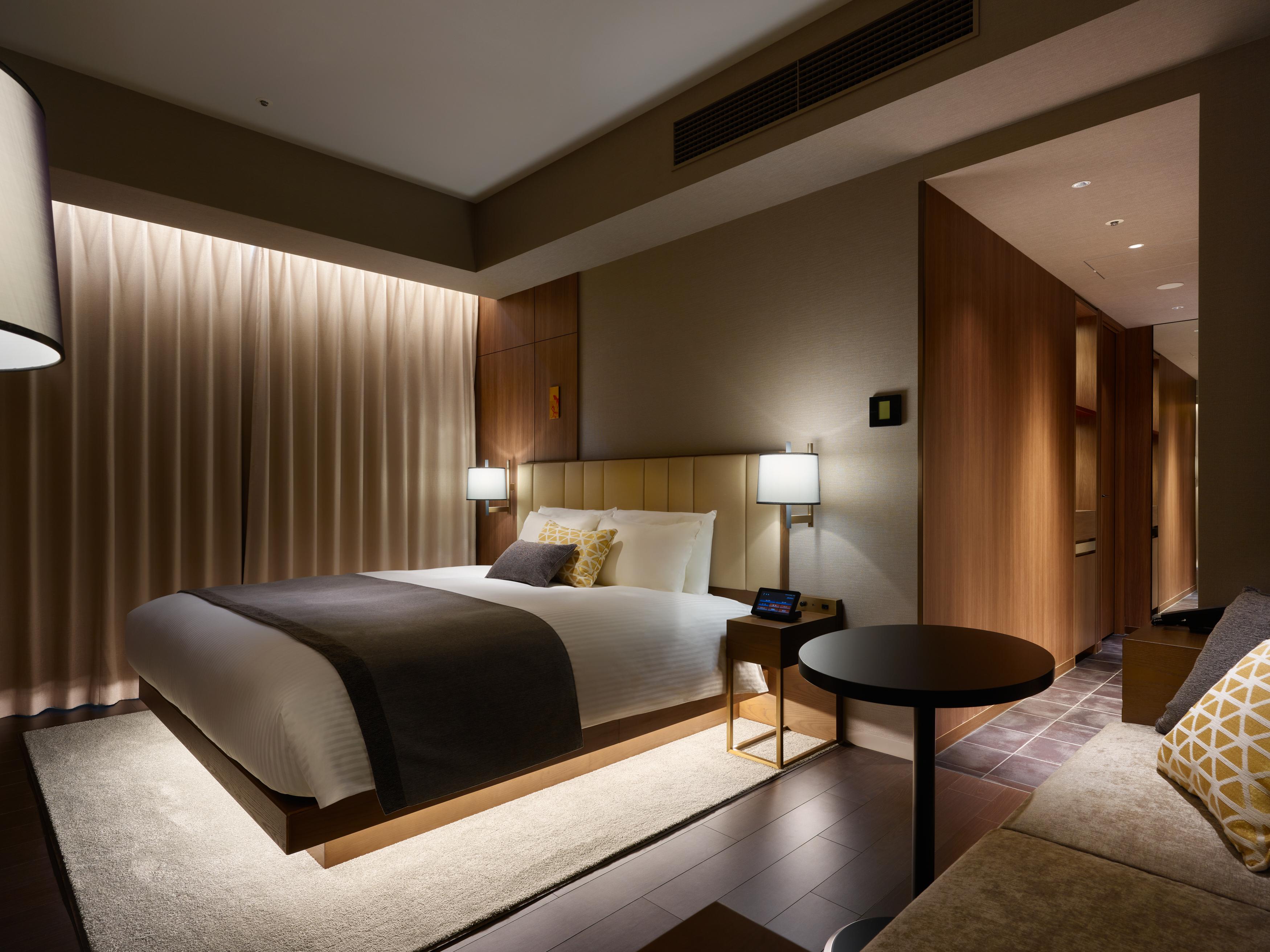 Mitsui Garden Hotel Roppongi Tokyo Premier Экстерьер фото The photo shows a modern hotel room featuring a king-sized bed with neutral-colored bedding and accent pillows. There are two bedside lamps on either side of the bed, providing a warm glow. The walls have a wood finish, and there's a soft area rug on