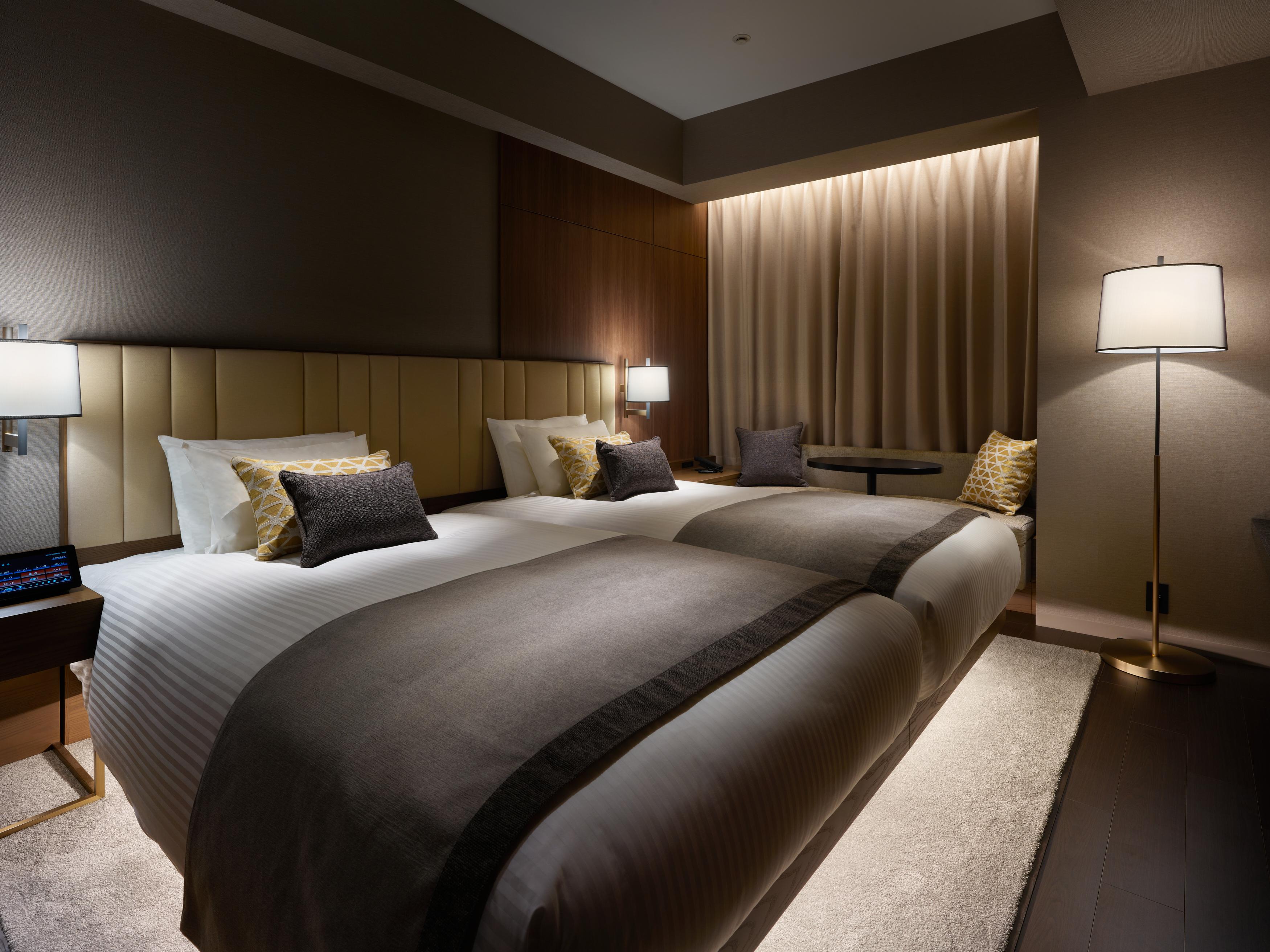 Mitsui Garden Hotel Roppongi Tokyo Premier Экстерьер фото The photo shows a modern hotel room featuring two beds with elegant bedding in neutral colors. Each bed is adorned with decorative pillows. The room has a sophisticated ambiance with dim lighting, highlighted by table lamps on either side of the beds