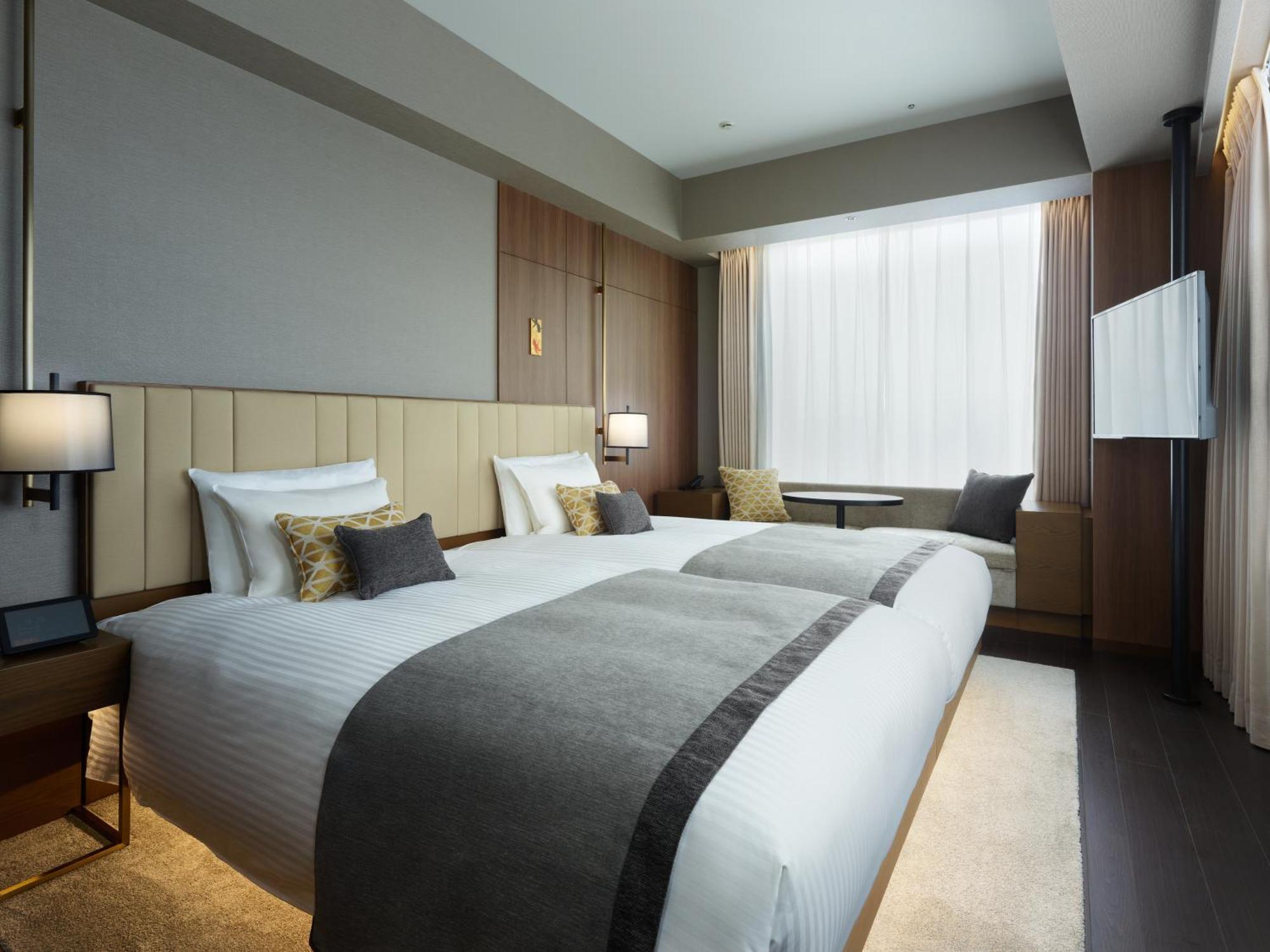 Mitsui Garden Hotel Roppongi Tokyo Premier Экстерьер фото The photo shows a modern hotel room featuring two beds with white linens and decorative pillows. The room has a minimalist design, with neutral-colored walls and wooden accents. Natural light comes in through large windows, which are partially covere