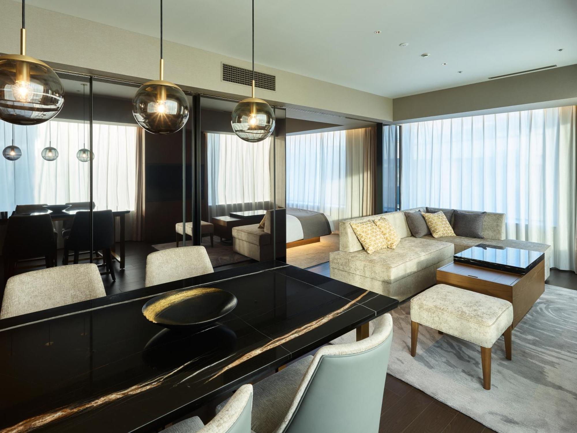 Mitsui Garden Hotel Roppongi Tokyo Premier Экстерьер фото The photo shows a modern and stylish living area. It features a dining table with elegant chairs, a comfortable seating area with a light-colored sofa, and a coffee table. The room is well-lit by large windows draped with sheer curtains, allowing nat